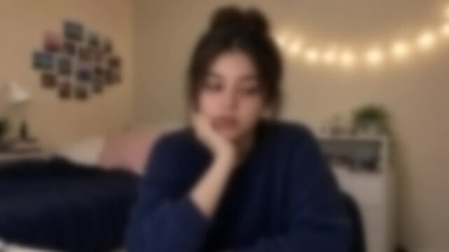 Young woman resting her chin on her hand during a video call in a dorm room, Full Gaussian Blur Abstract