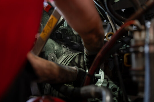 Mechanic wearing work gloves reaches between hoses and a guarded pulley assembly inside machinery, carrying out equipment servicing and mechanical maintenance