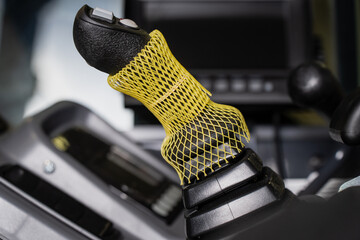 Machine control joystick with thumb buttons and a protective mesh sleeve inside an operator cab, representing manual equipment control and machinery operation © K