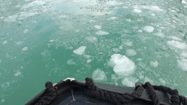 Small Boat Bow Moves Through Brash Ice in Svalbard Arctic Water. The bow of a compact inflatable boat cuts through green polar water filled with small ice fragments during a summer expedition.