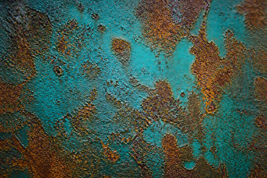 A close-up texture of weathered, rusted metal displaying patches of vibrant turquoise and deep orange-brown.