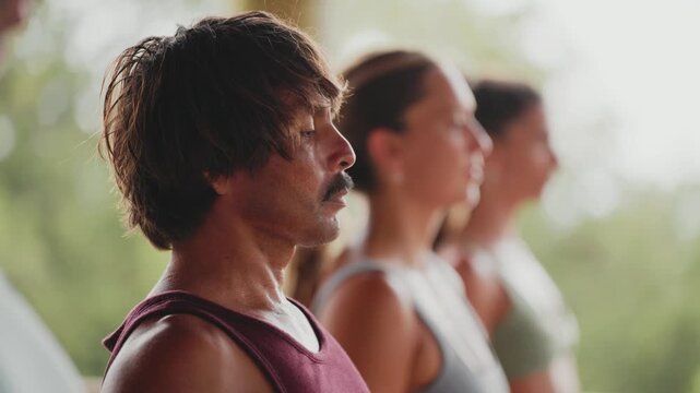 Side profile of a focused man with a mustache meditating in a group during a yoga class