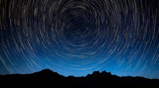 Star trails forming concentric circles above dark mountain ridge at night