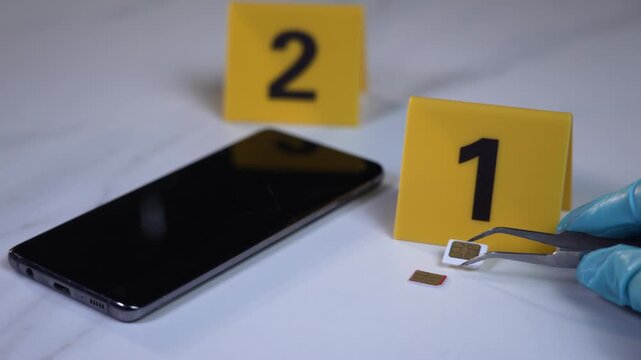Tweezers held by a gloved hand extract a SIM card between evidence markers one and two on a white marble table, high detail forensic mood, zooming close up shot