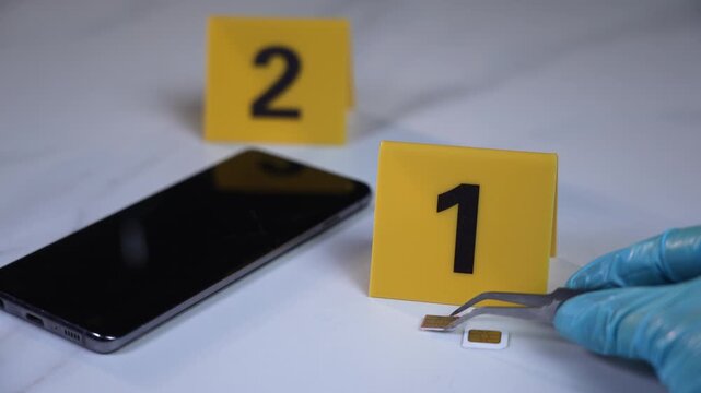 Gloved hand extracts SIM card with tweezers beside smartphone and evidence markers one and two, forensic investigation shot