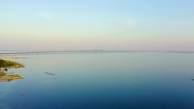Oresund bridge. Panoramic Drone footage of the cable-stayed span stretching across the calm strait at twilight, with the distant pylons silhouetted against a soft pastel sky. Drone footage