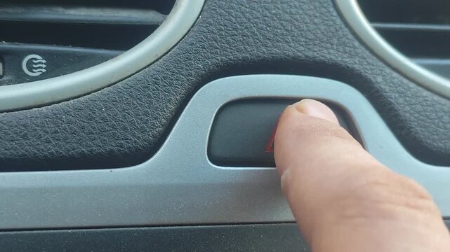 Man finger pressing hazard warning light button on car dashboard