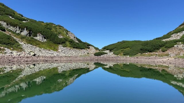 Scenic landscape of the crystal clear glacial Lake Mija with stunning mountain reflections in Parang Mountains, Romania. Nature and travel video, 4K, 60fps.