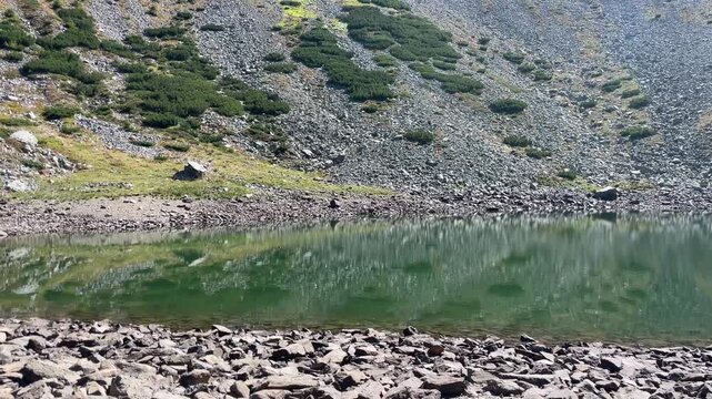 Panning shot of the emerald glacial Lake Mija and rocky alpine slope in Parang Mountains, Romania. Nature and travel video, 4K, 60fps.