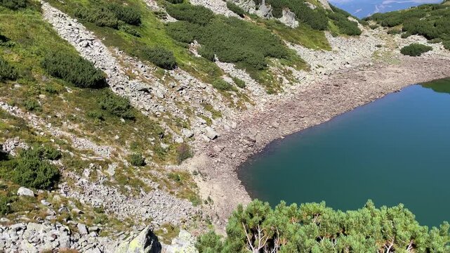 Panning shot of the emerald glacial Lake Mija and rocky alpine slope in Parang Mountains, Romania. Nature and travel video, 4K, 60fps.