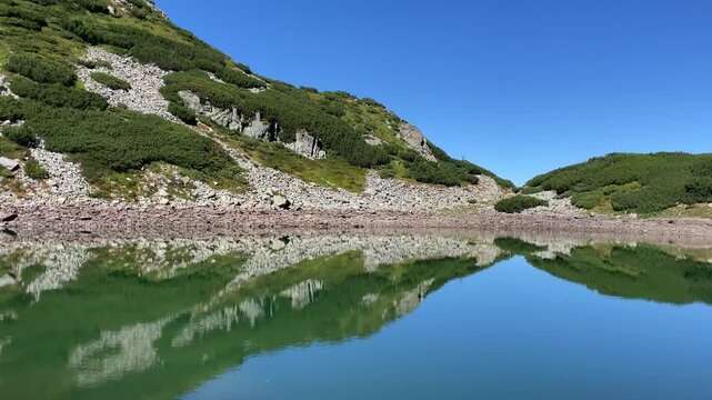 Panning shot of the emerald glacial Lake Mija and rocky alpine slope in Parang Mountains, Romania. Nature and travel video, 4K, 60fps.