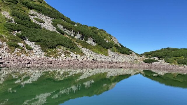 Panning shot of the emerald glacial Lake Mija and rocky alpine slope in Parang Mountains, Romania. Nature and travel video, 4K, 60fps.