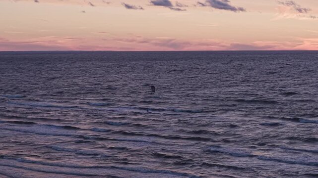 Lone kitesurfer rides dark Baltic waves beneath a glowing eclipse sunset