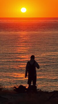 Lone visitor watches an orange sunset over Atlantic waters from Dune du Pilat, France, vertical static