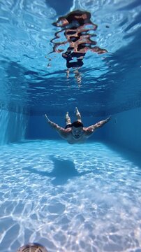 Underwater view of a man diving and swimming through a clear blue swimming pool, captured in super slow motion at 240 fps with beautiful light reflections.