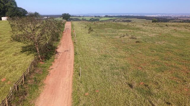 Aerial view of dirty road, agricultural fields and pasture in a sunny day