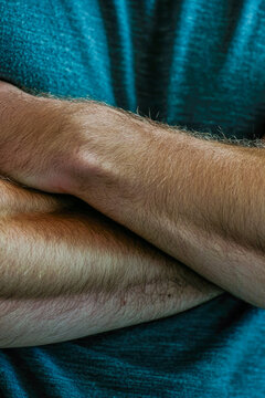 A close-up of a person with their arms crossed, looking serious or defensive. vertical frame
