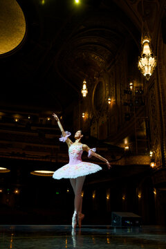 Ballerina balancing en pointe beneath ornate theater chandeliers