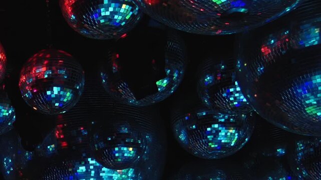 Dense disco ball cluster fills with multicolor club reflections. Numerous mirrored spheres crowd the frame while turquoise, red, gold, green and purple light moves across the surfaces.