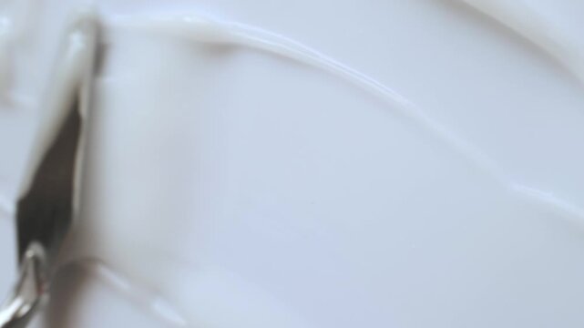 Spatula smearing white cosmetic cream, creating beautiful texture on plain background