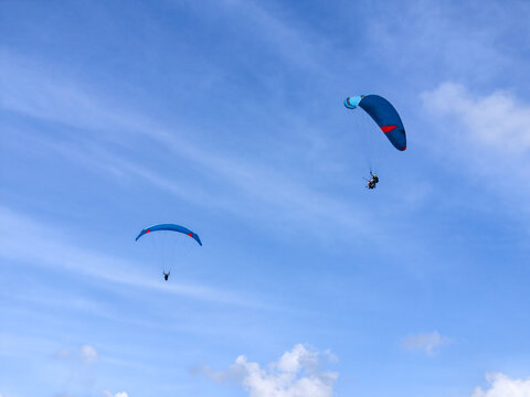 Two Paragliders Flying High in Clear Blue Sky with Light Clouds