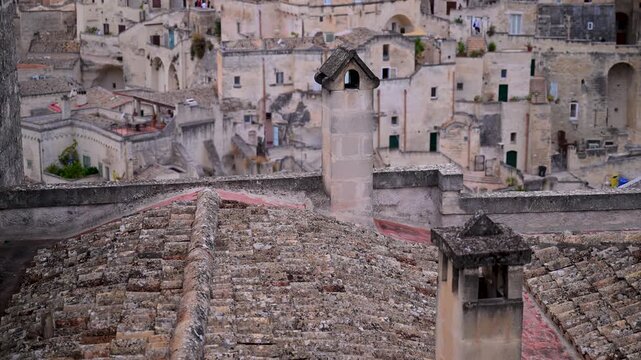 Old tiled rooftops and stone chimneys stand in front of densely packed cave dwellings in the historic Sassi di Matera district.