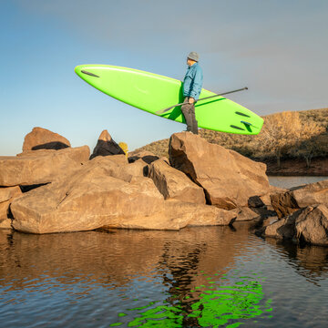 male paddler with an inflatable stand up paddleboard on a rocky shore of mountain lake - Horsetooth Reservoir in northern Coloradod