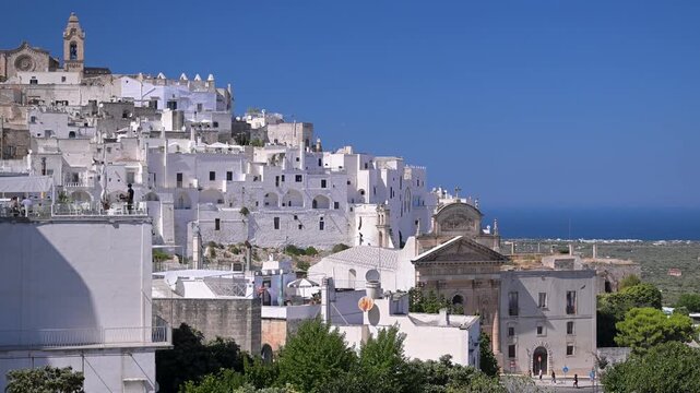 Historic Old Town of Ostuni Citt&agrave; Bianca climbs the hillside above a distant Adriatic horizon under deep blue sky.