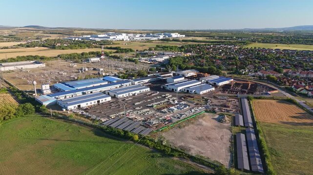 G&ouml;d, Hungary electric substation and battery factory with power lines, warehouses, roads and nearby housing in an industrial suburban landscape, aerial view.