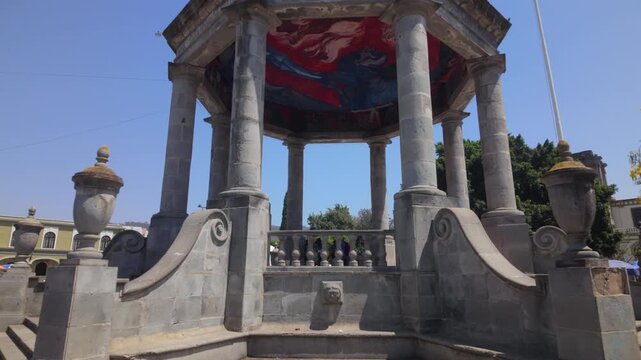 Dolly in toward a historic stone gazebo in a sunny Ciudad Guzman Jalisco plaza, ideal for travel, architecture, and town square footage.