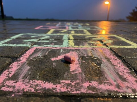 Hopscotch chalk game on wet pavement at dusk with glowing streetlight