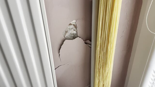 Close-up of a cracked interior wall with broken plaster and visible structural damage near a window, representing home repair, renovation, construction defects and property damage.