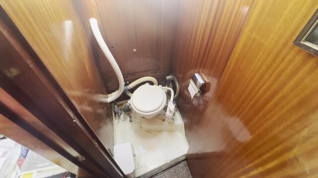 Compact marine toilet inside a wooden sailboat cabin, showing practical bathroom facilities, onboard living, sailing lifestyle and nautical interior design.
