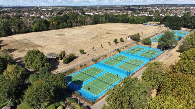 4K UHD drone orbit shot panning around a scenic tennis court complex nestled next to green trees and a traditional cricket pitch at Raphael Park, Romford, England