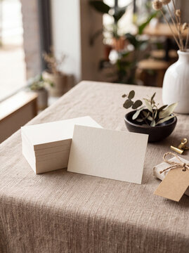 Stack of blank textured ivory cards with a single card mockup displayed on a neutral linen table alongside kraft tags and botanical accents.