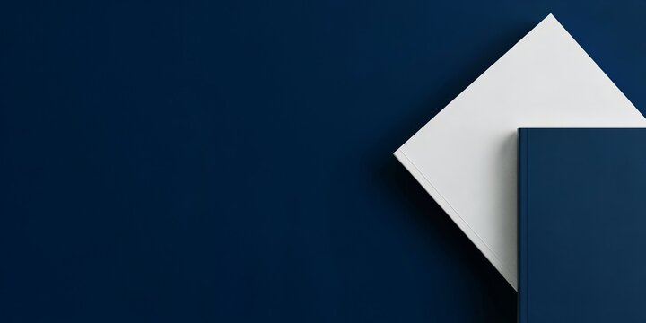 A white rectangular paper sheet placed diagonally on a deep dark blue background, creating a minimalist composition with sharp geometric angles and a strong contrast between the two solid colors