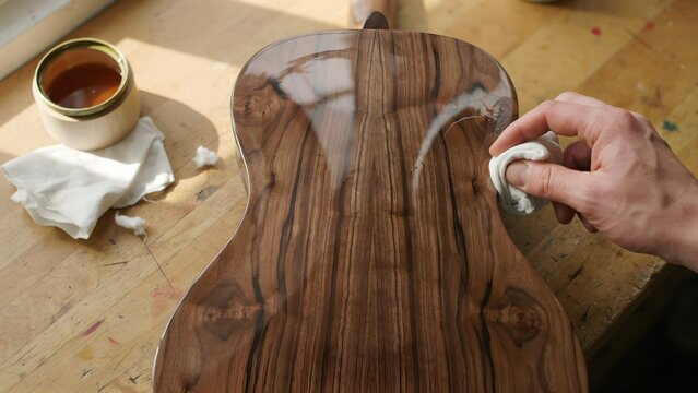 Skilled artisan polishing wooden guitar body with cloth in workshop setting