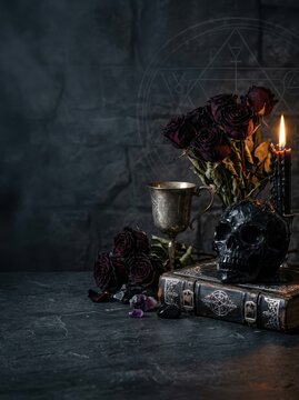 Occult Still Life with Obsidian Skull, Antique Spellbook, and Dried Black Roses on Dark Stone with Copy Space