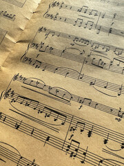 Fototapeta premium Close up of old sheet music with musical notes and clefs. Old musical score - no lyrics. Atmospheric music background with notes on old brown paper. Image of a sheet of music with notes. Scrapbooking