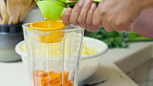 Hands squeezing fresh lime juice using a green manual press into a blender