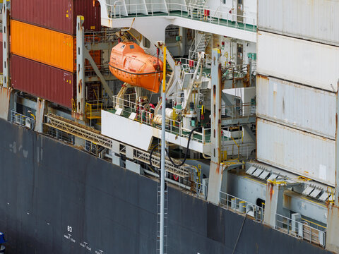 Orange Lifeboat Secured on the Side of a Large Container Ship During Daytime Operations at a Port