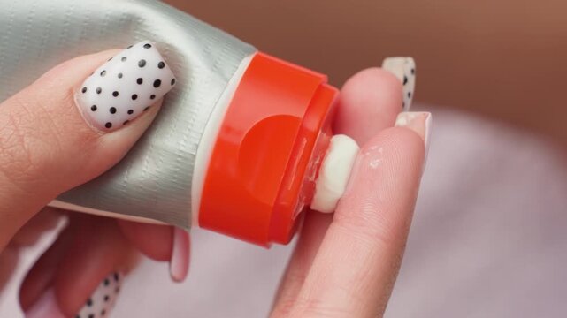 Close up view of hands with white nail polish featuring black polka dots applying cream from tube to skin. focus remains on detailed textures and actions related to skincare or manicure