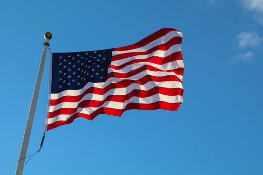 American flag waving on white pole against clear blue sky