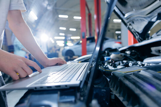 Hands typing on laptop over open engine in auto repair shop