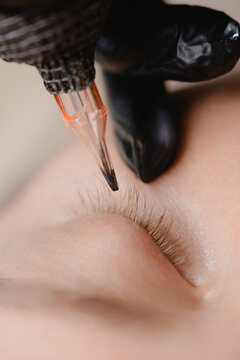 Eyelash technician tattooing lashes on reclining client face. Concept microblading permanent beauty procedure