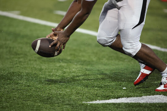 Close up of a football player reaching down to grab the ball on the field, A football player in uniform is about to pick up the ball during a game on a green grass field