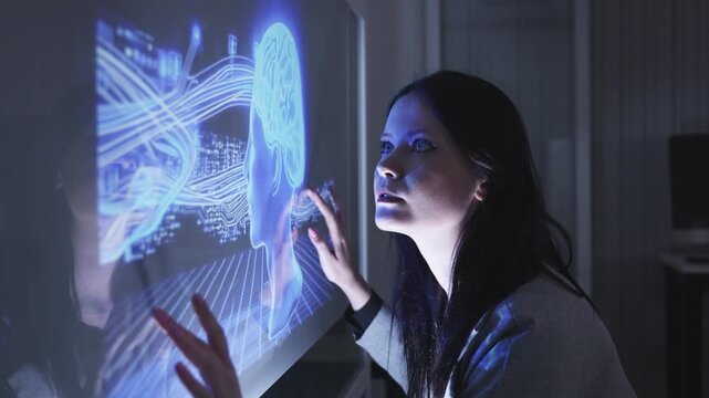 Businesswoman touches a glowing blue holographic brain diagram on a transparent screen, symbolizing AI, neuroscience, or digital intelligence technologies.