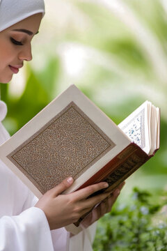 A woman sits quietly reading a book while wearing a flowing white robe. vertical frame
