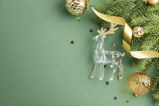 Christmas holiday decorations festive arrangement with clear reindeer ornament and golden ribbon on green background