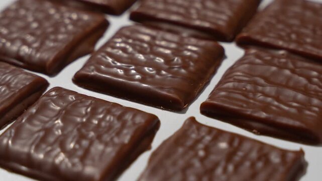 Individual chocolate-covered crackers are arranged in a grid on a white background and slowly rotate together, shown in extreme macro close-up.